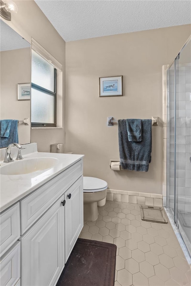 bathroom featuring a shower with door, vanity, a textured ceiling, tile patterned flooring, and toilet