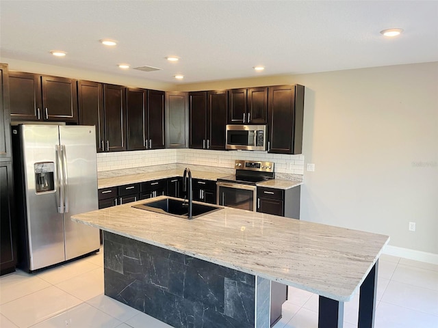 kitchen featuring a kitchen island with sink, backsplash, light tile patterned floors, sink, and appliances with stainless steel finishes