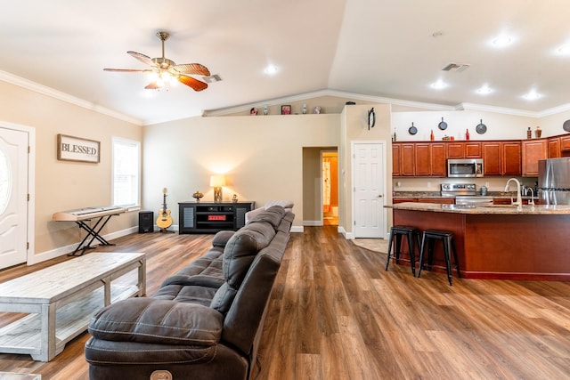 living room featuring vaulted ceiling, wood-type flooring, ornamental molding, sink, and ceiling fan