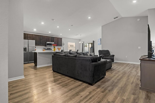 living room featuring vaulted ceiling, an inviting chandelier, and light hardwood / wood-style floors