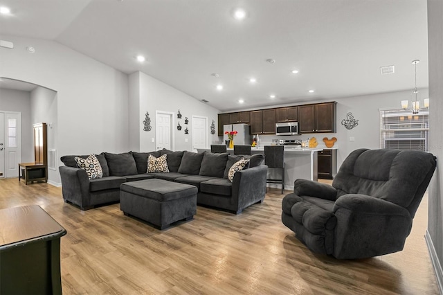 living room featuring light wood-type flooring, lofted ceiling, and a chandelier