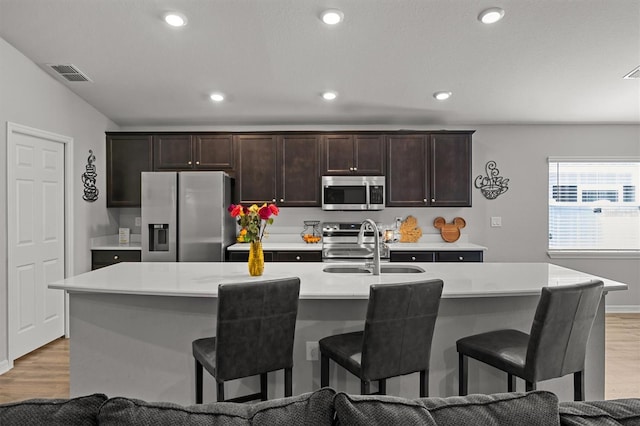 kitchen with stainless steel appliances, light hardwood / wood-style floors, a kitchen island with sink, and a breakfast bar