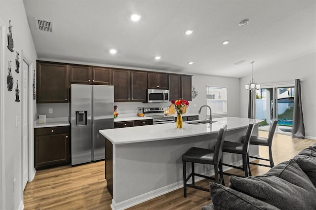 kitchen featuring a kitchen island with sink, stainless steel appliances, sink, lofted ceiling, and light wood-type flooring