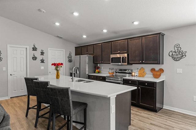 kitchen with a kitchen island with sink, light wood-type flooring, a breakfast bar, appliances with stainless steel finishes, and lofted ceiling