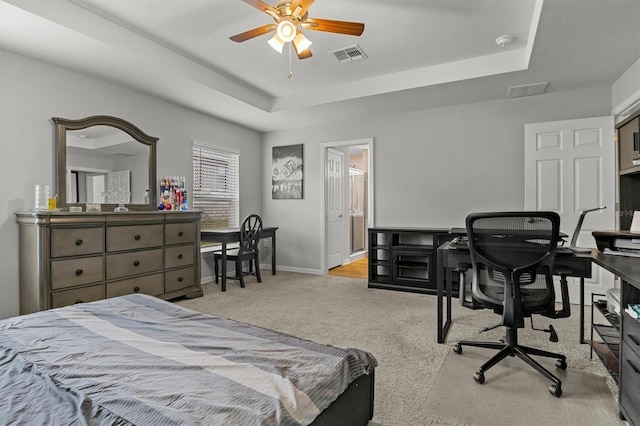 bedroom with light colored carpet, connected bathroom, a raised ceiling, and ceiling fan