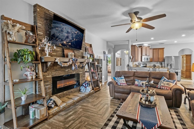 living room featuring a stone fireplace, ceiling fan, and light parquet floors