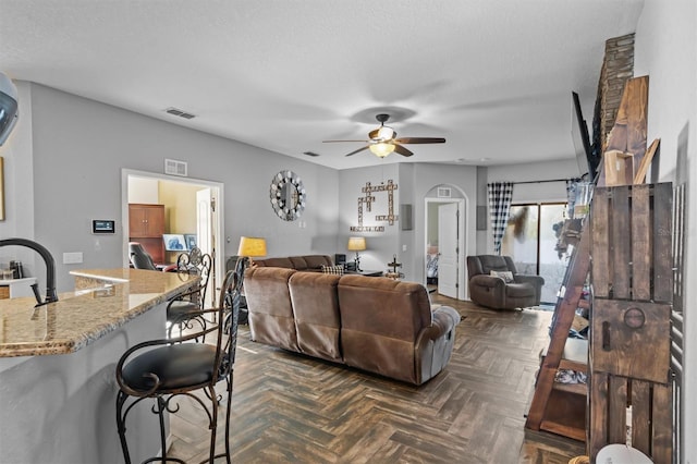 living room featuring ceiling fan, dark parquet floors, and a textured ceiling