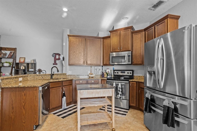 kitchen featuring stainless steel appliances, a peninsula, a sink, visible vents, and brown cabinets