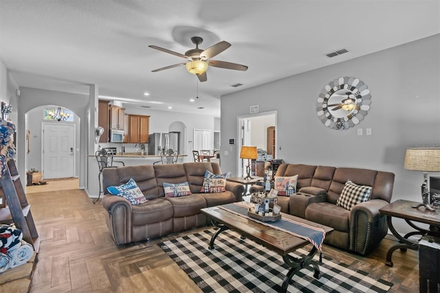living area featuring arched walkways, visible vents, and a ceiling fan