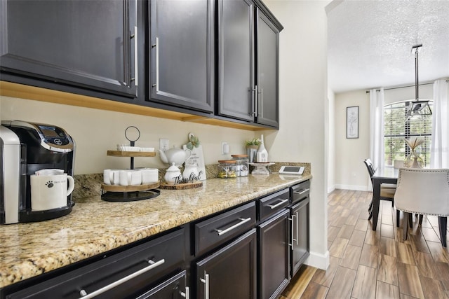 kitchen featuring a textured ceiling, decorative light fixtures, a chandelier, and light stone countertops