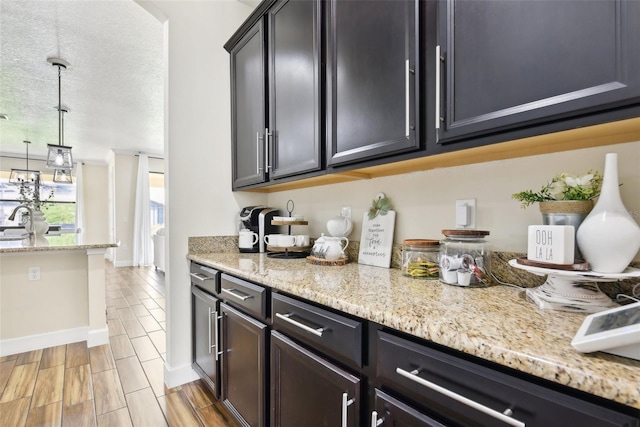 kitchen with pendant lighting, a textured ceiling, sink, and light stone countertops