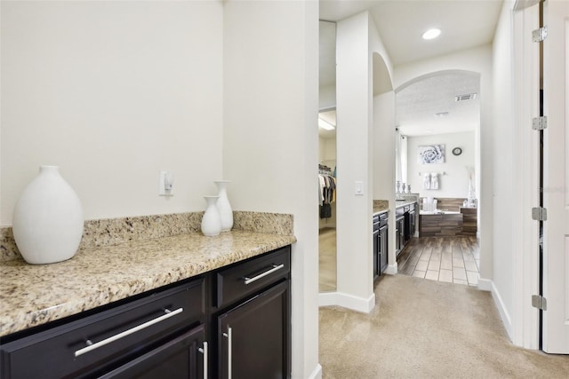 bar with a textured ceiling, light colored carpet, and light stone countertops