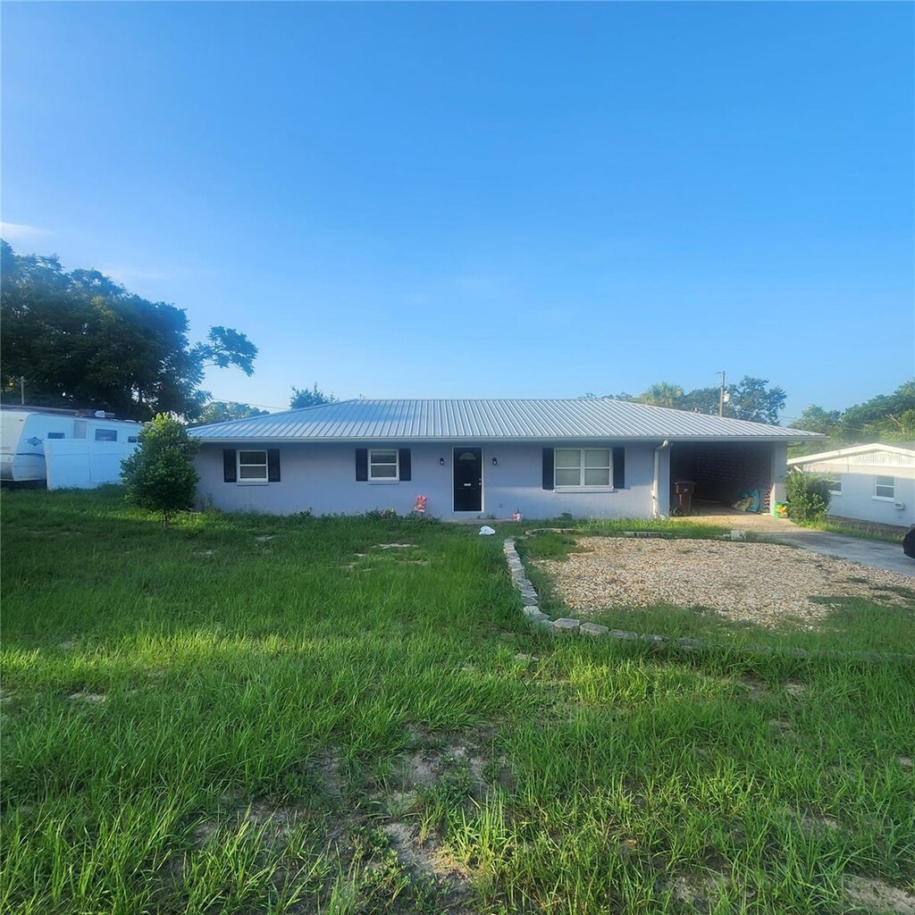 ranch-style home with an attached carport, stucco siding, metal roof, and driveway
