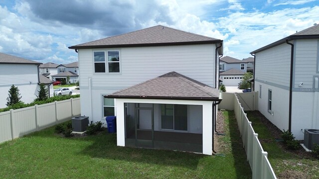 rear view of property featuring central AC unit and a lawn