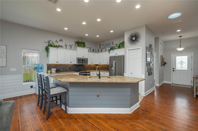 kitchen with dark hardwood / wood-style flooring, appliances with stainless steel finishes, a kitchen island with sink, sink, and white cabinetry