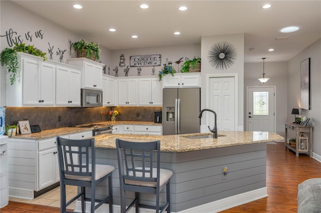 kitchen with a kitchen island with sink, decorative light fixtures, appliances with stainless steel finishes, white cabinets, and light hardwood / wood-style floors