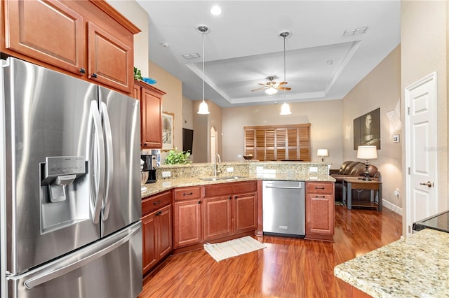 kitchen with stainless steel appliances, wood-type flooring, sink, ceiling fan, and a raised ceiling