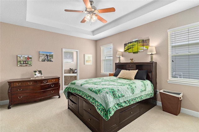 bedroom featuring a raised ceiling, light colored carpet, and ceiling fan