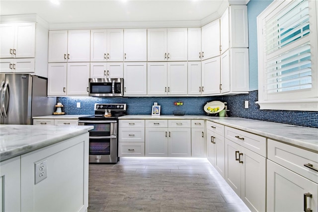 kitchen with light wood-type flooring, white cabinets, appliances with stainless steel finishes, and light stone counters