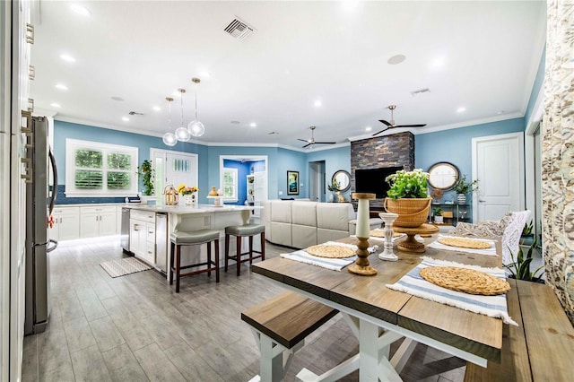 dining room with ceiling fan, a fireplace, light hardwood / wood-style floors, and ornamental molding