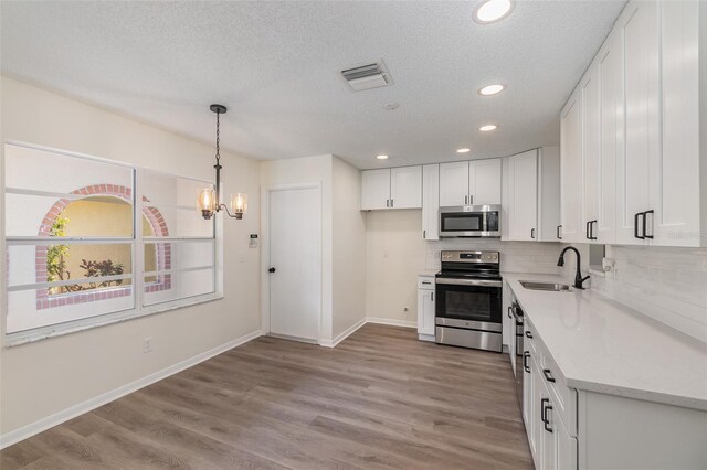 kitchen featuring a textured ceiling, stainless steel appliances, sink, white cabinetry, and light wood-type flooring