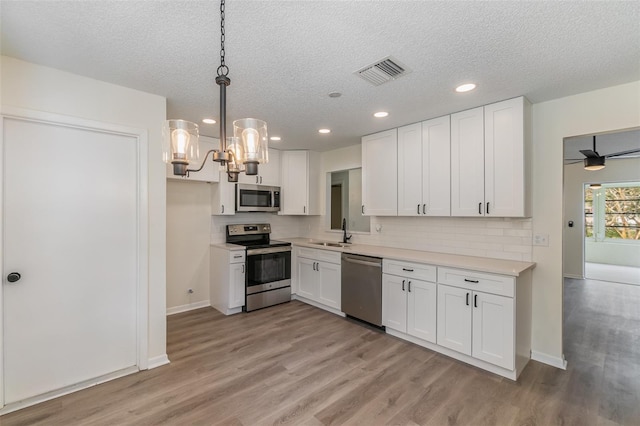 kitchen with appliances with stainless steel finishes, white cabinetry, and hanging light fixtures