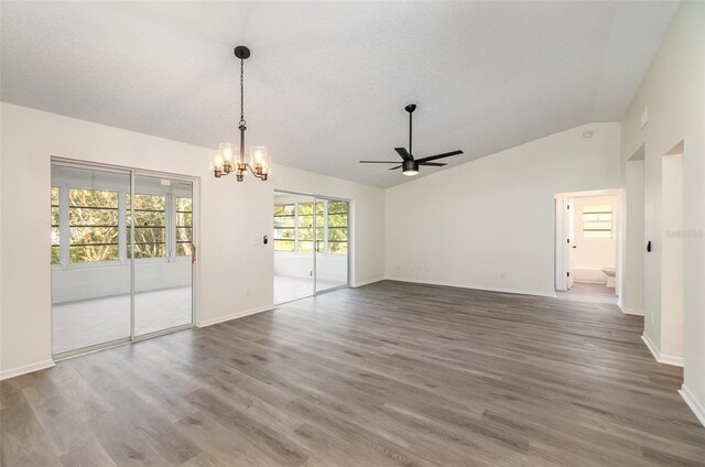 spare room featuring lofted ceiling, ceiling fan with notable chandelier, wood-type flooring, and a textured ceiling