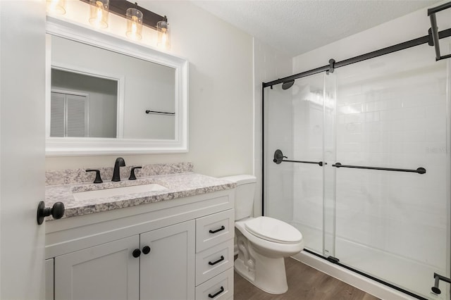 bathroom featuring toilet, an enclosed shower, vanity, a textured ceiling, and hardwood / wood-style flooring