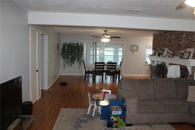 living room featuring a brick fireplace, dark wood-type flooring, and ceiling fan