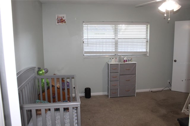 carpeted bedroom featuring a nursery area, a ceiling fan, and baseboards