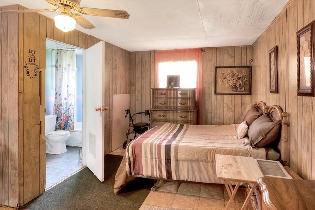 carpeted bedroom with wooden walls, ensuite bath, and ceiling fan