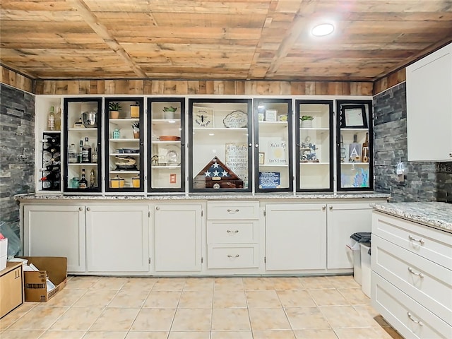 kitchen featuring light stone counters, white cabinets, wooden walls, light tile patterned floors, and wooden ceiling