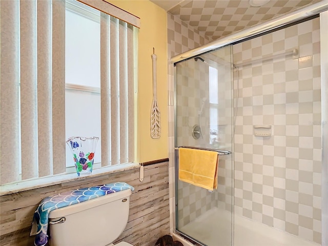 bathroom featuring wooden walls, toilet, and a shower with shower door