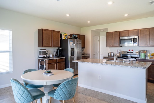 kitchen featuring a kitchen island with sink, light tile patterned floors, light stone counters, sink, and appliances with stainless steel finishes