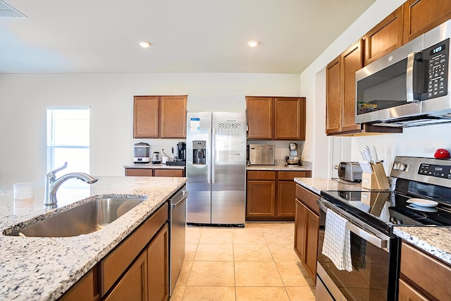 kitchen with light tile patterned floors, sink, light stone countertops, and appliances with stainless steel finishes