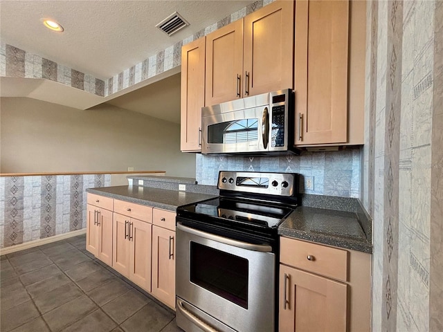 kitchen featuring a textured ceiling, dark tile patterned floors, stainless steel appliances, and decorative backsplash