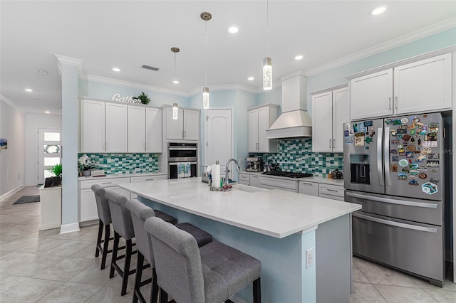 kitchen with appliances with stainless steel finishes, a kitchen bar, premium range hood, and a kitchen island with sink