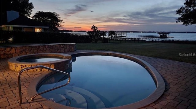 pool at dusk with an in ground hot tub and a water view