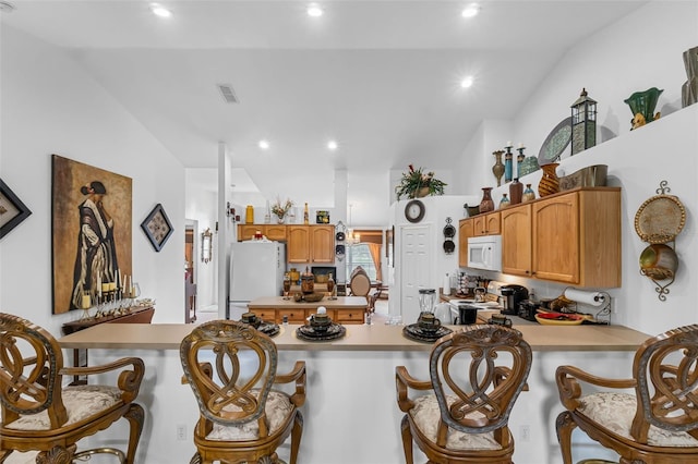 kitchen with a kitchen bar, white appliances, kitchen peninsula, and lofted ceiling