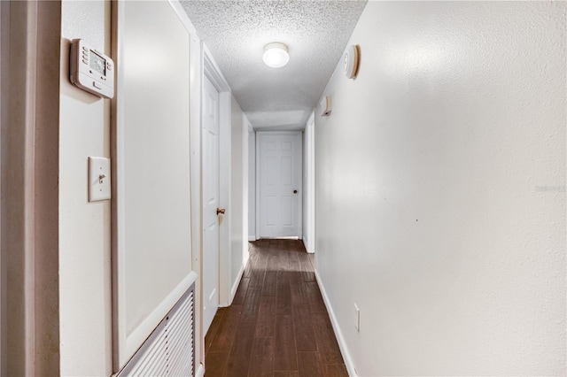 corridor with dark wood-style flooring, baseboards, and a textured ceiling