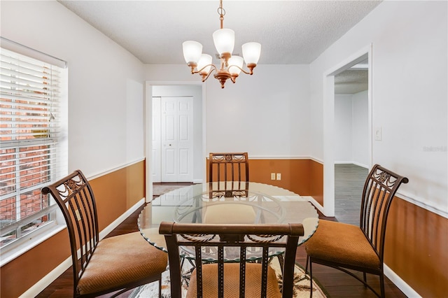 dining room with baseboards, a textured ceiling, wood finished floors, and a notable chandelier