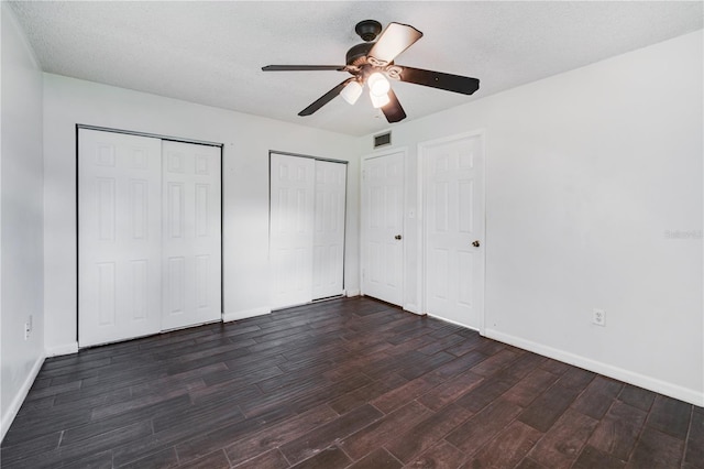 unfurnished bedroom with dark wood-style flooring, a textured ceiling, visible vents, two closets, and baseboards