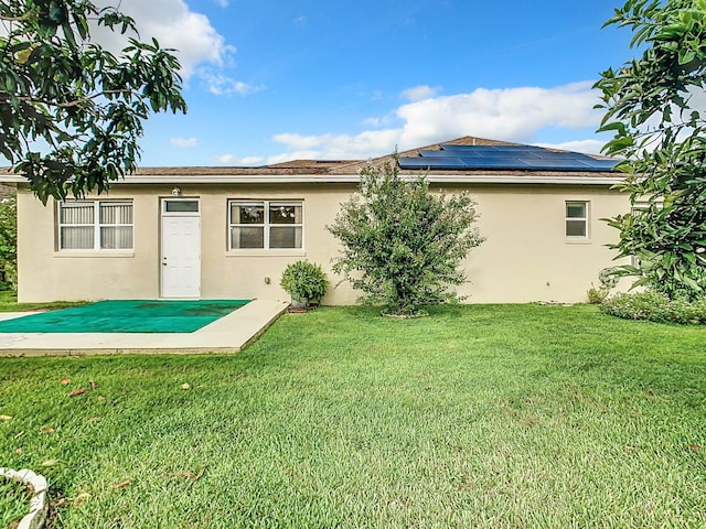 back of house featuring stucco siding, solar panels, and a yard