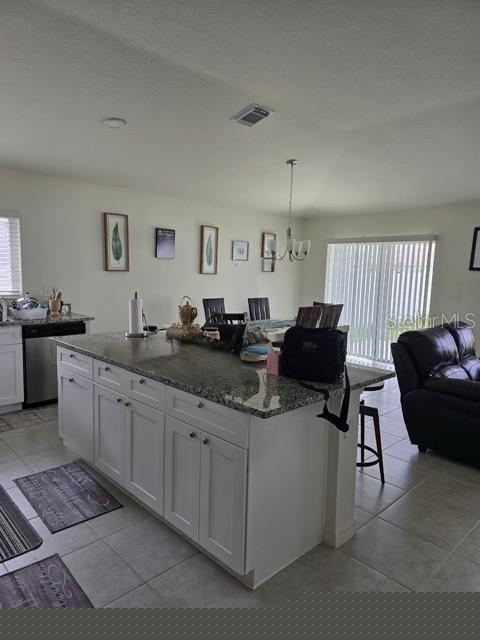 kitchen with hanging light fixtures, dishwasher, stone countertops, white cabinetry, and an island with sink