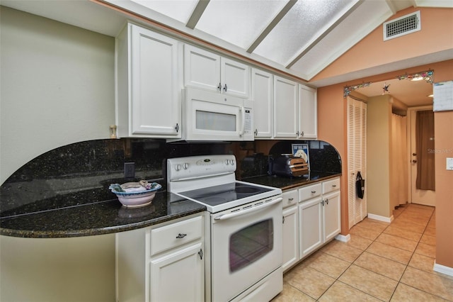 kitchen with dark stone counters, white appliances, white cabinetry, and lofted ceiling