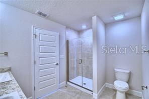 bathroom with a shower with door, vanity, a textured ceiling, tile patterned flooring, and toilet