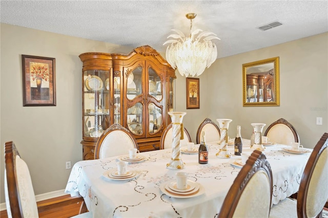 dining area with wood-type flooring, an inviting chandelier, and a textured ceiling