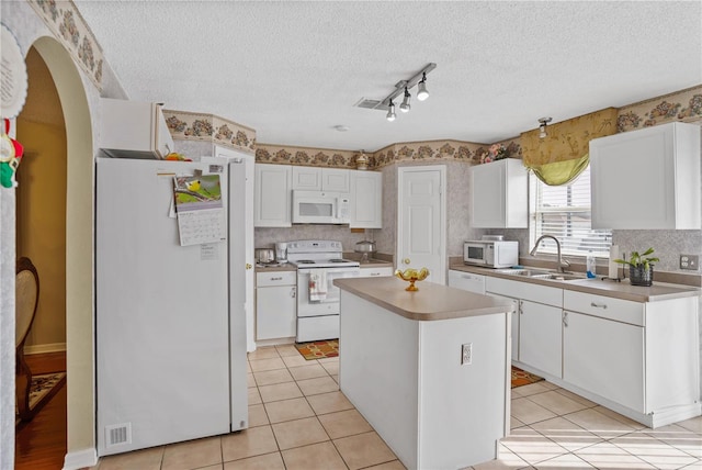 kitchen with white appliances, a kitchen island, sink, and white cabinets