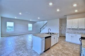 kitchen featuring white cabinetry, stainless steel appliances, sink, light stone countertops, and a center island with sink