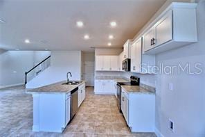 kitchen with appliances with stainless steel finishes, a center island with sink, white cabinetry, and sink